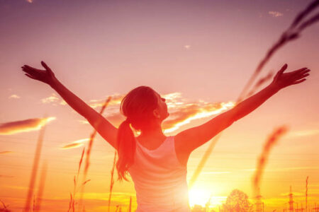 femme regardant le soleil couchant, les bras en corix